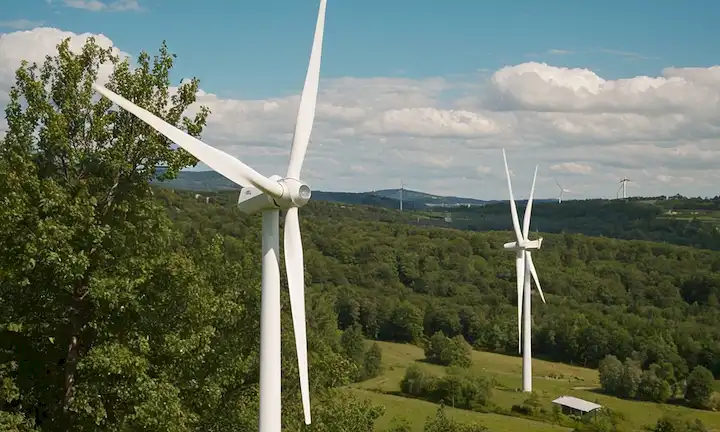2-3 turbinas de viento residenciales, diferentes tamaños y formas, vegetación en el fondo, soleado cielo con nubes blancas, árboles o colinas a la distancia, posiblemente un medidor de potencia o controlador cercano