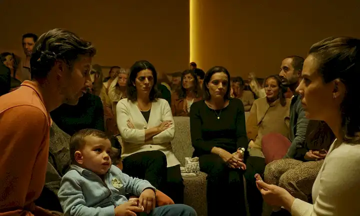Grupo de personas discutiendo las causas y los impactos sociales en la producción de bebés en España. La discusión rodea el problema de Baby Crack donde los niños no nacen debido a factores económicos, sociales y culturales como el acceso a servicios de salud, educación y planificación familiar.