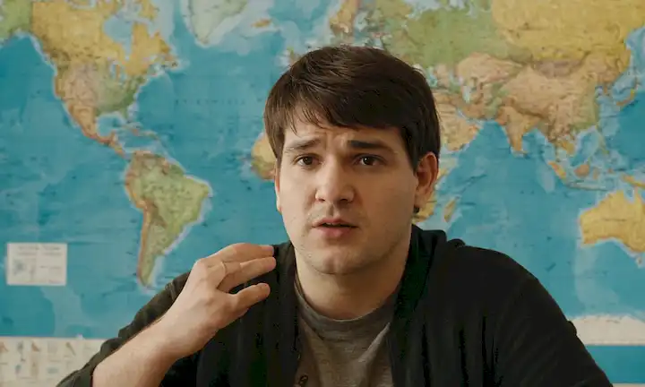 Una persona con síndrome de Tourettes hablando con confianza frente a un mapa mundial.