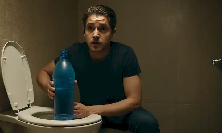 Una persona que sostiene una botella de agua sobre un tanque de baño con un aspecto preocupado.