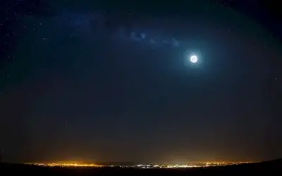 Una silueta iluminada por una luna tenue rodeada de éter sin estrellas con el título Contaminacion Lumnica exhibido en un panel electrónico entre. La imagen podría ser la representación artística de la atmósfera de la Tierra llena de contaminación o paisaje natural de noche con cielo oscuro y estrellas perdidas.