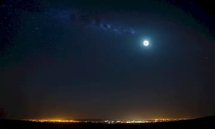 Una silueta iluminada por una luna tenue rodeada de éter sin estrellas con el título Contaminacion Lumnica exhibido en un panel electrónico entre. La imagen podría ser la representación artística de la atmósfera de la Tierra llena de contaminación o paisaje natural de noche con cielo oscuro y estrellas perdidas.