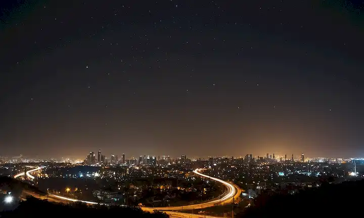 Luces de la ciudad iluminadas en medio del aire contaminado, contrastando con un cielo celeste claro, mostrando la naturaleza interconectada de elementos urbanos y astronómicos. (Traducción literal a las consecuencias de un cielo brillante: un impacto multifacético de la contaminación de la luz: el skyline nocturno se oscurece, las estrellas desaparecen).