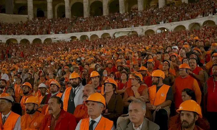 Un grupo de personas con chalecos de seguridad y cascos como cámara dentro del Coliseo muestra temperaturas que aumentan a niveles mortales. La película Alerta Roja (Red Alert) es proyectada para el público, concientizando sobre temas climáticos globales que provocan temperaturas extremas en algunas ciudades como Roma.