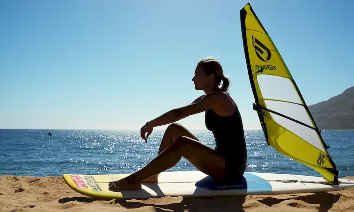 Windsurfer sentado, simbolizando la función marina de protección deportiva en la promoción de la conciencia ambiental y las acciones responsables. Una silueta de un surfista se encuentra en un fondo azul oceánico mientras que el texto anuncia Lamadrid como Campeona del Windsurf y Embajadora de la Protección Marina con Ecomar.