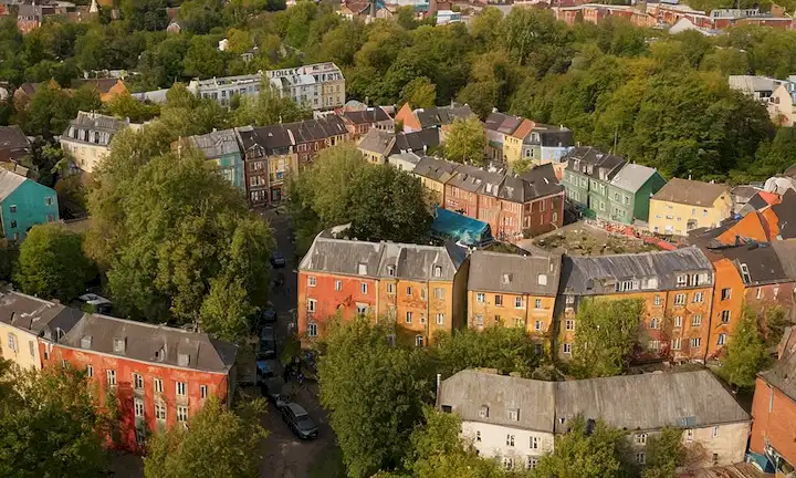 Vista aérea del colorido y bohemio barrio de Christiania, contrastado con los ambientes urbanos y eslóganes anti-establecimiento en una ciudad frente a disturbios relacionados con las drogas. Este libro sigue la evolución de esta comunidad única amenazada por el crimen y las drogas, explorando sus problemas sociales y su resistencia.