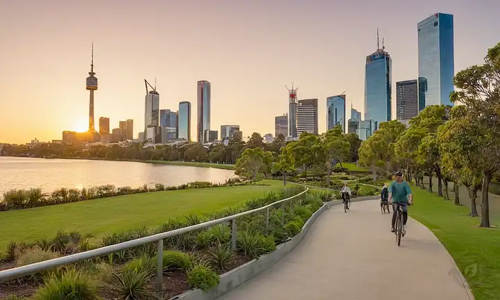 parque lleno de vegetación, gente sonriente, vibrante arte callejero, emblemáticos monumentos como la Torre Eureka, jardines urbanos, ruta de bicicletas, puesta del sol detrás de paisaje urbano, vista lago o río