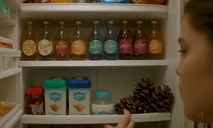 Cubos de hielo en una nevera, estantes apilados con bebidas y aperitivos, decoraciones temáticas de invierno como copos de nieve o pinos, aire frío girando hacia fuera, persona que llega a tomar algo