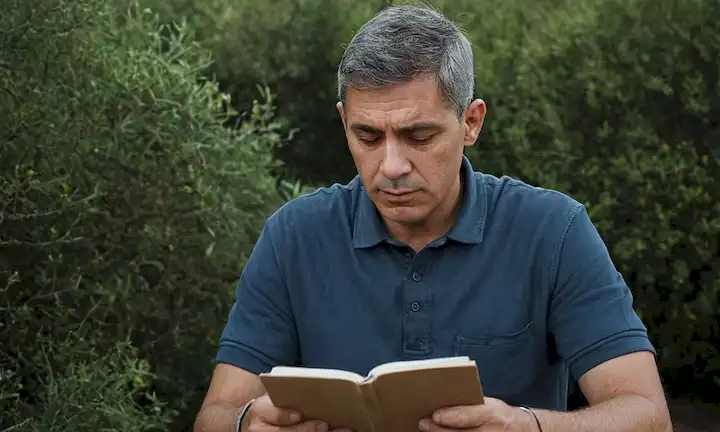 Hombre leyendo un libro con una mirada sombría y conflictiva en su cara mientras sostiene un bolígrafo y papel. El texto está escrito en inglés y menciona la opinión de Grays de que existe un conflicto inherente entre humanos y naturaleza, junto con el conflicto en curso en Gaza.