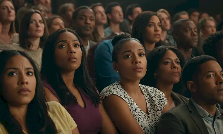 Una multitud de género mixto viendo una película con diferentes reacciones que reflejan debates sobre representación y racismo en la industria cinematográfica.