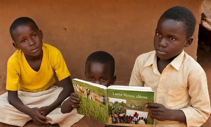 Young boy sharing a homemade photo album with pictures of daily life in Uganda along detailed captions about the local culture and its significance to childrens lives. La imagen muestra su hogar, escuela, actividades familiares, y un vistazo a la vida cotidiana en Uganda, a través de un objetivo personal único donde Sami narra la historia y comparte sus experiencias desde la perspectiva de un joven en esta vibrante comunidad.