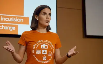 Persona usando una camiseta naranja mientras da una presentación sobre la inclusión digital como catalizador para el cambio. El texto La Inclusión Digital Como Motor De Cambio aparece por encima de su cabeza