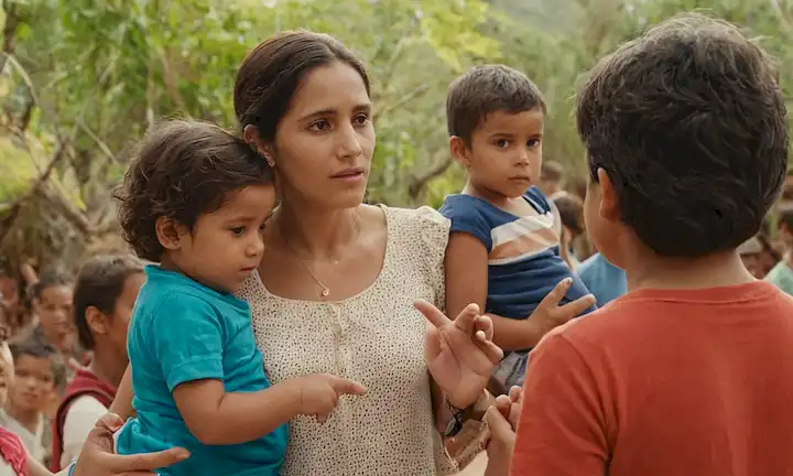 Una joven con sus hijos hablando en manos, rodeada de gente ayudándose durante el día. La frase una historia de esperanza y cambio (una historia de esperanza y cambio) combina elementos relacionados con la maternidad, el crecimiento personal, la unidad y la perseverancia, destacando la historia de la vida de María Galáns como un modelo de rol impactante para las generaciones futuras.