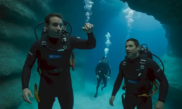 Buceo Oceanógrafo con traje de alta tecnología en profundo sistema de cuevas. Compañeros de equipo animando desde líneas laterales en el entorno de laboratorio submarino, discutiendo especies de tiburón y rayos águila recién descubiertas. (Esta es una declaración bastante larga de un párrafo condensada según sea necesario para adaptarse al formato solicitado.)