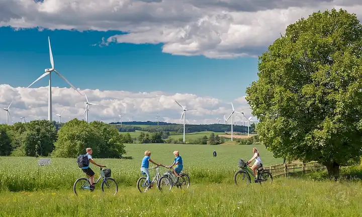 Bosques verdes, colinas rodantes, prados soleados, invernaderos, turbinas eólicas, paneles solares, cielo azul con nubes blancas, árboles frondosos, bicicletas, gente sonriente, mano sosteniendo una hoja, reservas naturales, transporte sostenible, hogares ecológicos, economía circular, niños felices jugando al aire libre