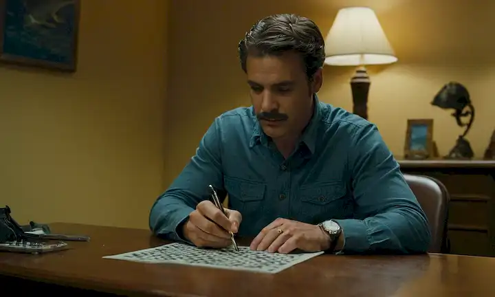 Hombre sentado en un escritorio, completando un crucigrama con pistas sobre biología marina e investigación. Sin embargo, hay un misterio para resolver que implica la vida marina en peligro y las amenazas al proyecto. Esto está escrito en un formato de novela detective de estilo inglés, no una revista científica o publicación científica como La reproducción del pez Luna de Pez Luna: El gigante del océano en peligro.