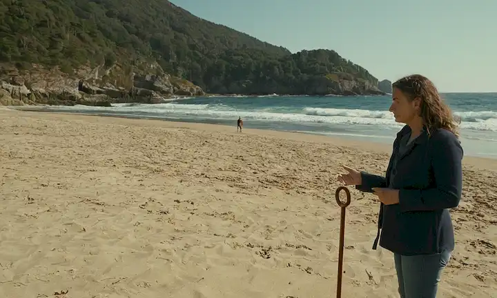 Persona de pie cerca de un paraguas de playa ya que explican sobre residuos plásticos y desafíos que enfrentan en regiones costeras como Galicia y Asturias debido a su uso en playas.