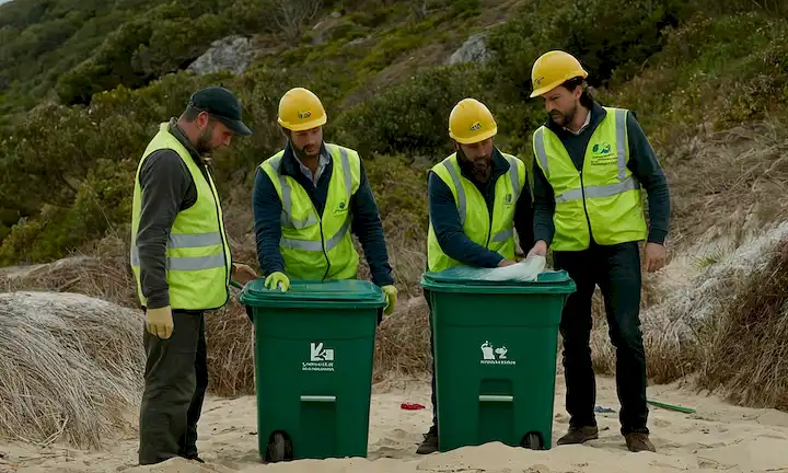 Un grupo de trabajadores que construyen una basura bioplásica verde puede utilizar técnicas sostenibles en las regiones costeras, mientras que otros problemas de gestión de residuos persisten como basura y sobreutilización de bolsas de plástico de uso único. El subtítulo español podría ser algo en las líneas del viaje hacia la sostenibilidad de los plásticos biodegradables: Playas de Galicia y Asturias todavía afectados.