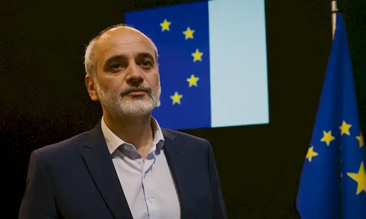 Una foto del director de Indras frente a una presentación del proyecto Galileo, con bandera autónoma de Europa.