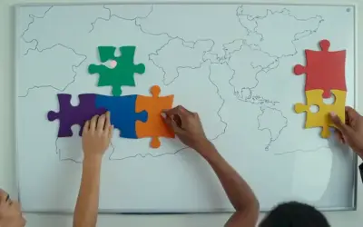 Objetivos y metas globales mostrados en una pizarra con diversas manos sosteniendo piezas de rompecabezas alrededor de ella.