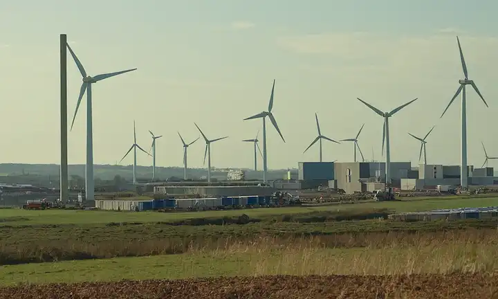 Turbinas eólicas siendo desmanteladas, piezas reciclables siendo separadas, una fábrica o un almacén en el fondo, cuchillas recicladas transformadas en nuevos productos, un futuro paisaje sostenible con granjas eólicas a distancia, personas trabajando juntas para lograr objetivos ambientales